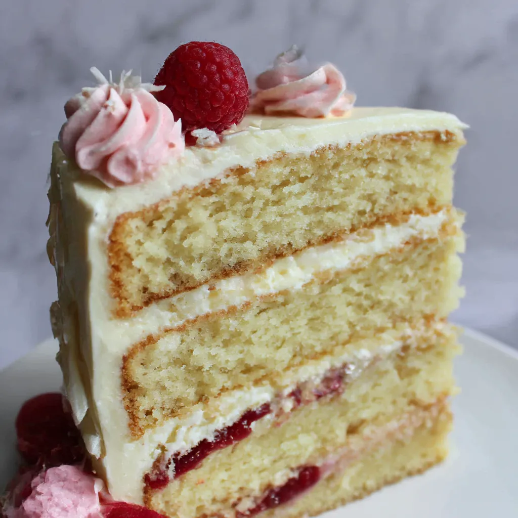 A slice of coconut cake with raspberries on top.
