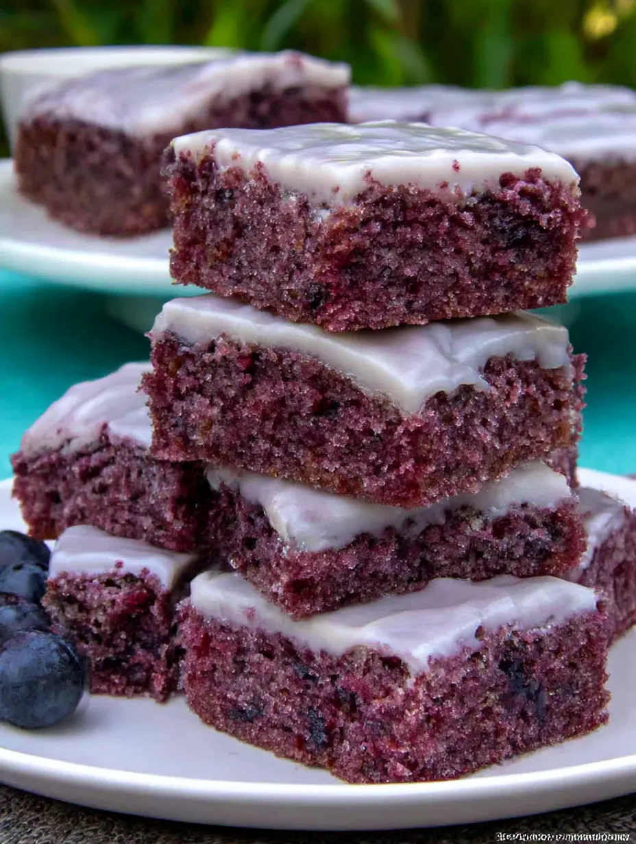 A stack of brownies with white frosting and blueberries.