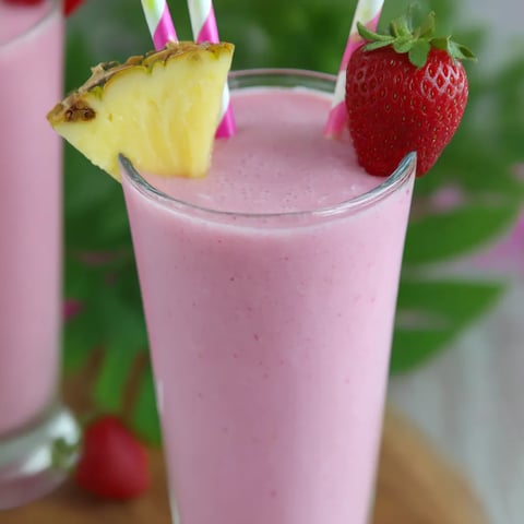 A glass of pink drink with a pineapple wedge and a strawberry on top.